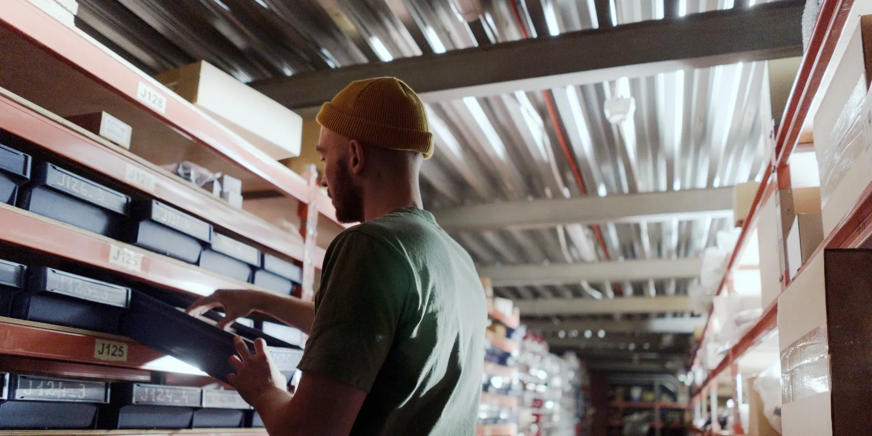 Worker pulls a labelled parts drawer from a shelf in a stock room